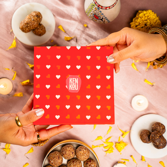 Red gift box with heart patterns held by hands on a festive background with candles and decorative items.